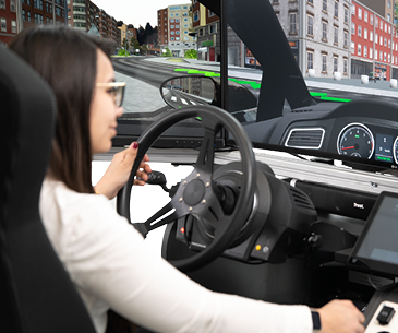 Fahrsimulator testen Frau sitzt in einem Fahrsimulator mit Lenkrad und virtueller Stadtumgebung auf dem Bildschirm