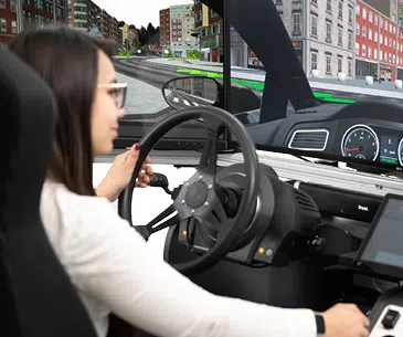Fahrsimulator testen Frau sitzt in einem Fahrsimulator mit Lenkrad und virtueller Stadtumgebung auf dem Bildschirm